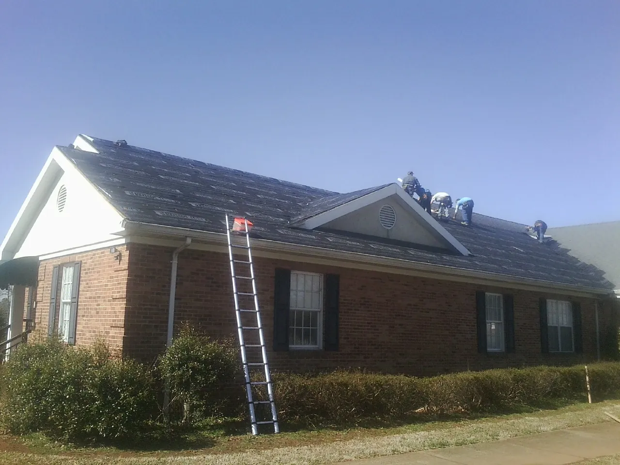 Crew tearing shingles off a brick ranch roof with a ladder set — Emergency Roof Repair work by our crew in Oakville