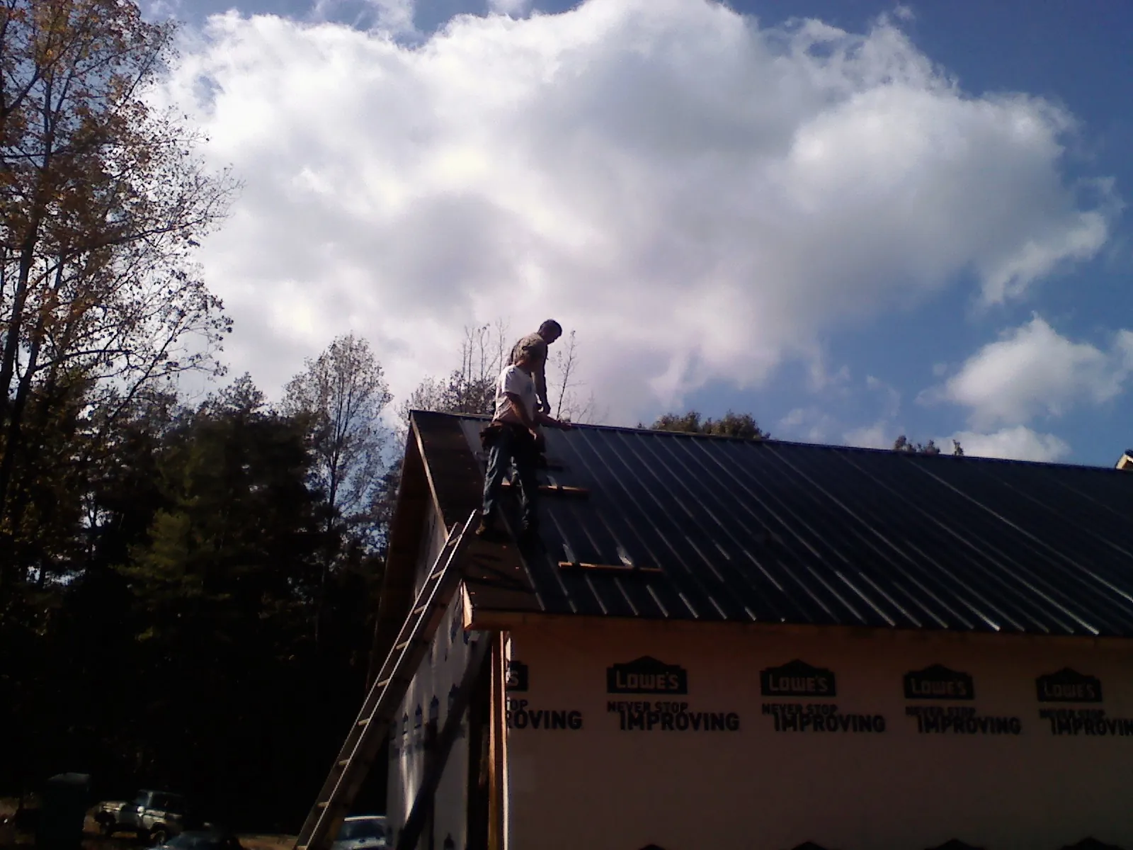 Roofer fastening dark metal panels high against a cloudy sky, from a Roof Inspection job in Oakville
