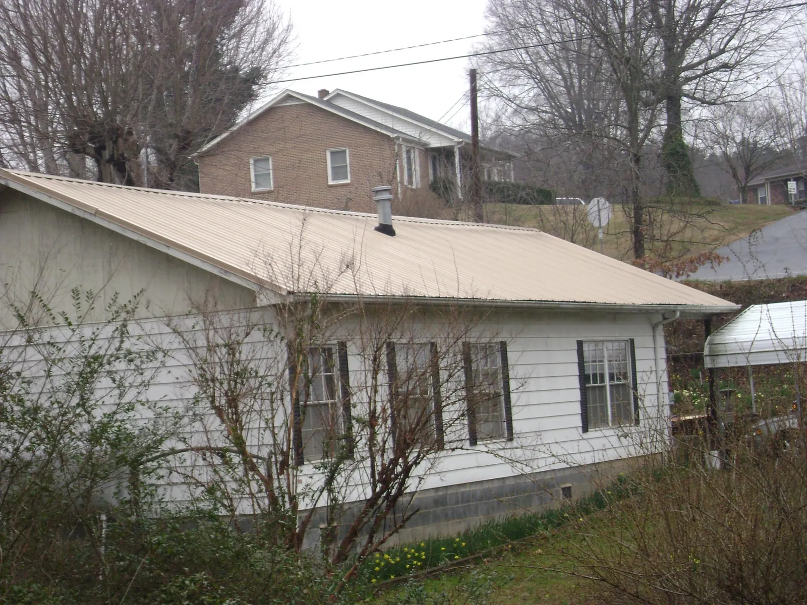 Tan metal roof on a white sided house set into a hillside — Commercial Roofing by Roofing Brothers in Oakville